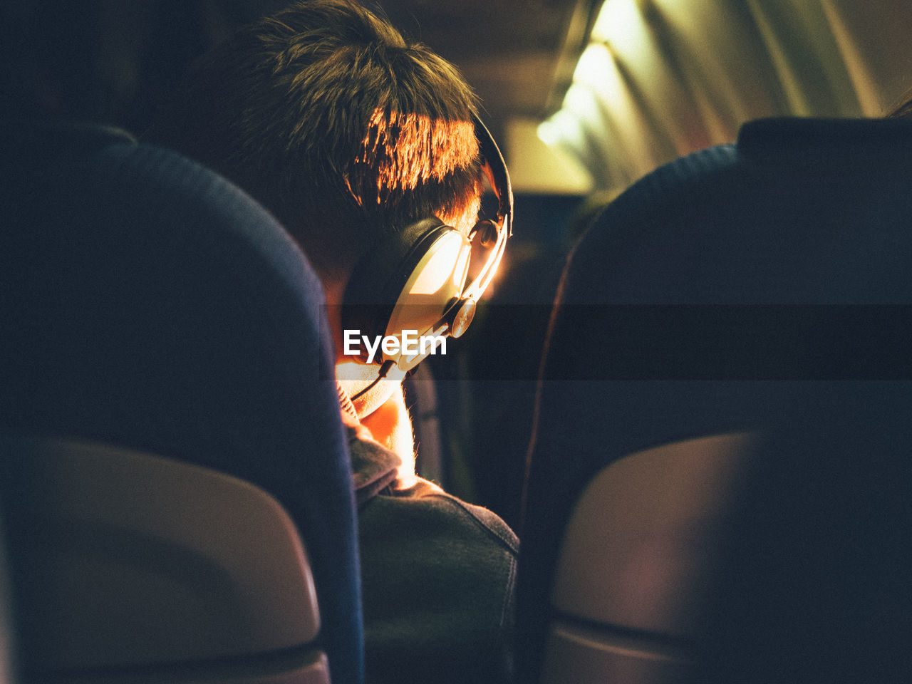Rear view of man sitting in airplane while listening music