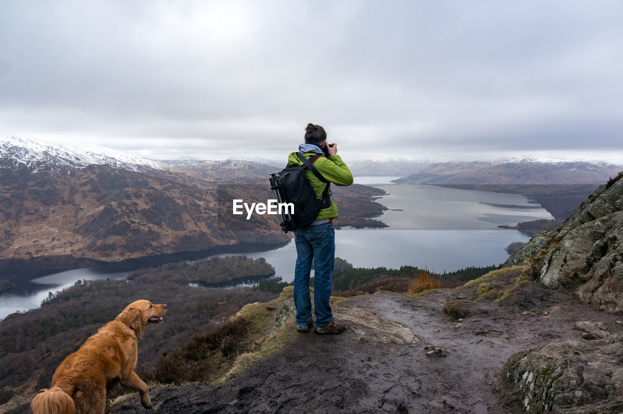 Rear view of woman standing with dog on cliff against valley
