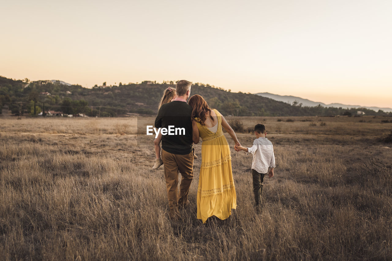Young family holding hands while walking away in california field