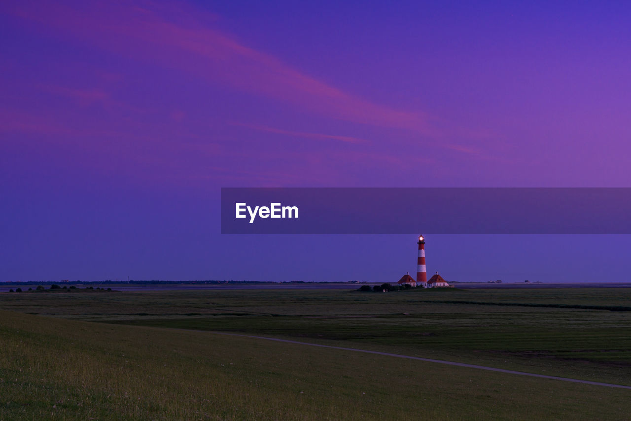Lighthouse on field against sky at dusk