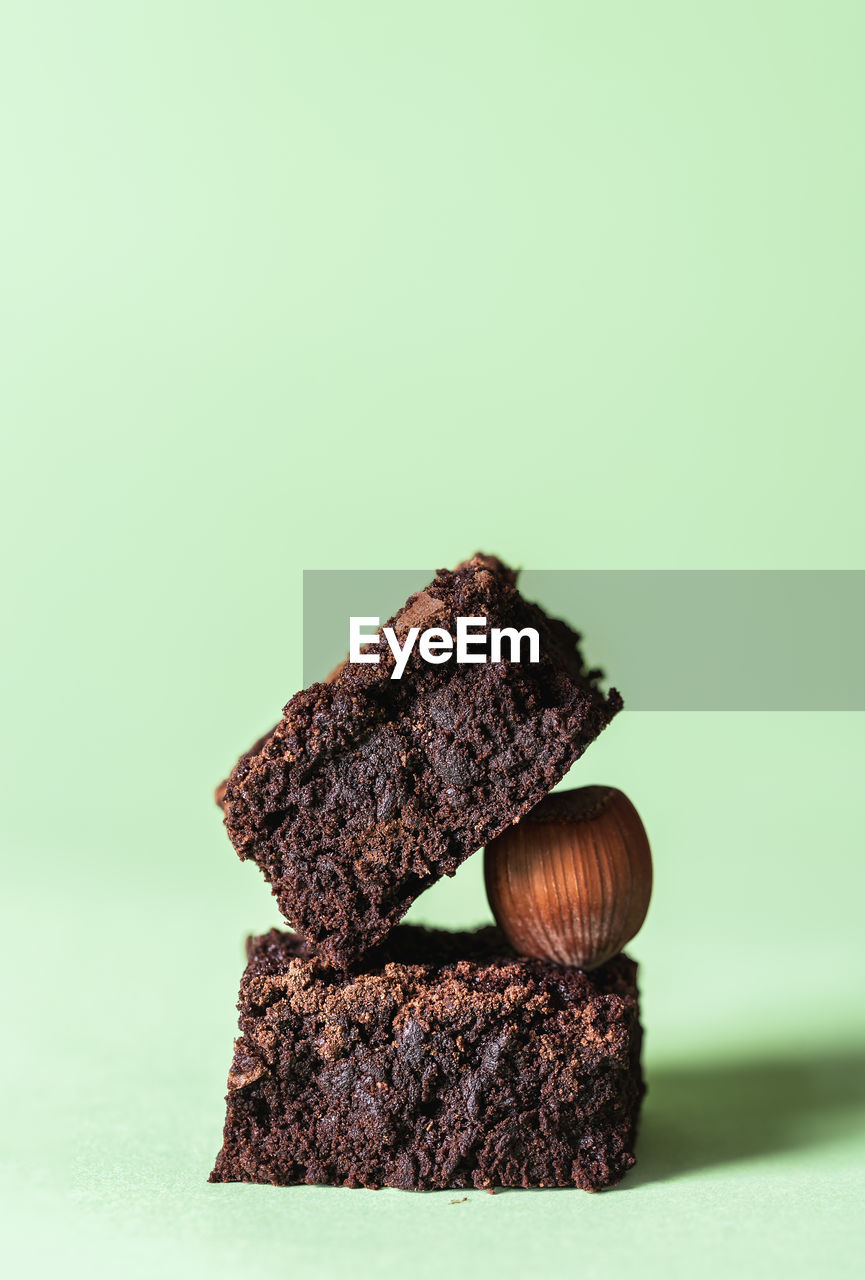 Stack of two dark chocolate brownies and a hazelnut, on a mint green background. chocolate cake.