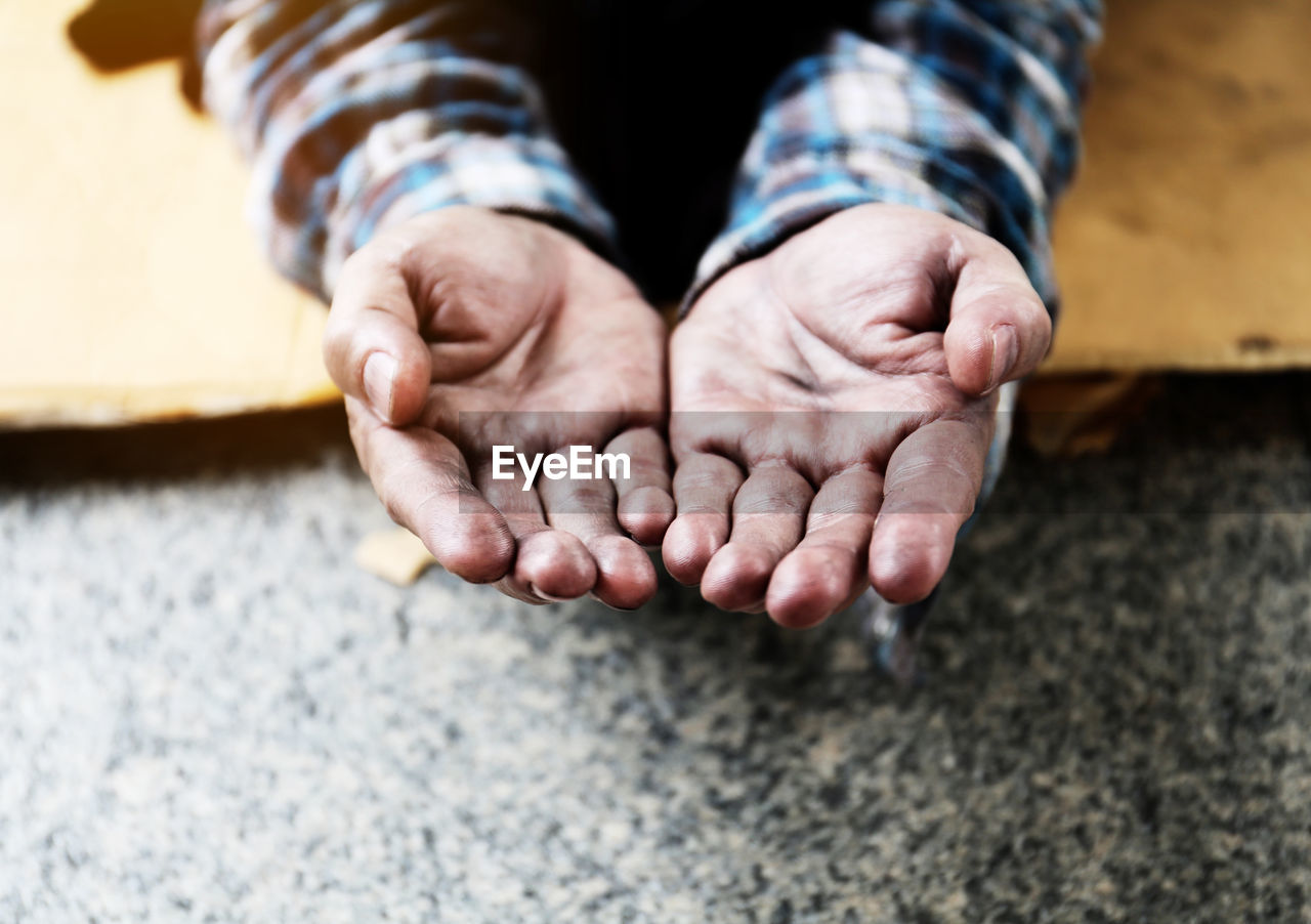Cropped hands of mature man begging on floor