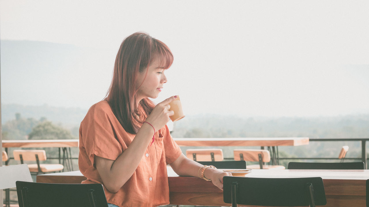 Woman drinking coffee in cup on table against sky