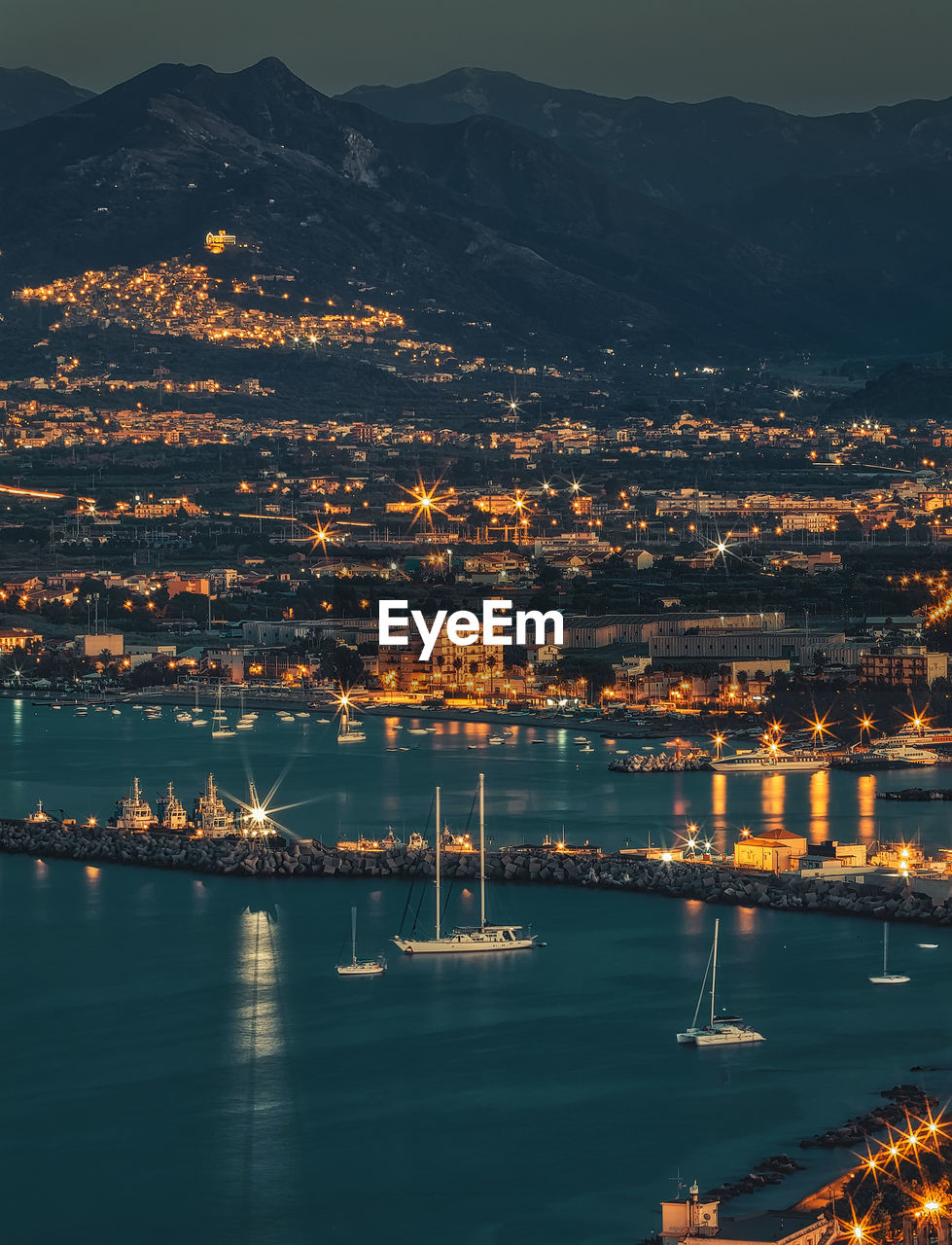 Illuminated city by sea against sky at night