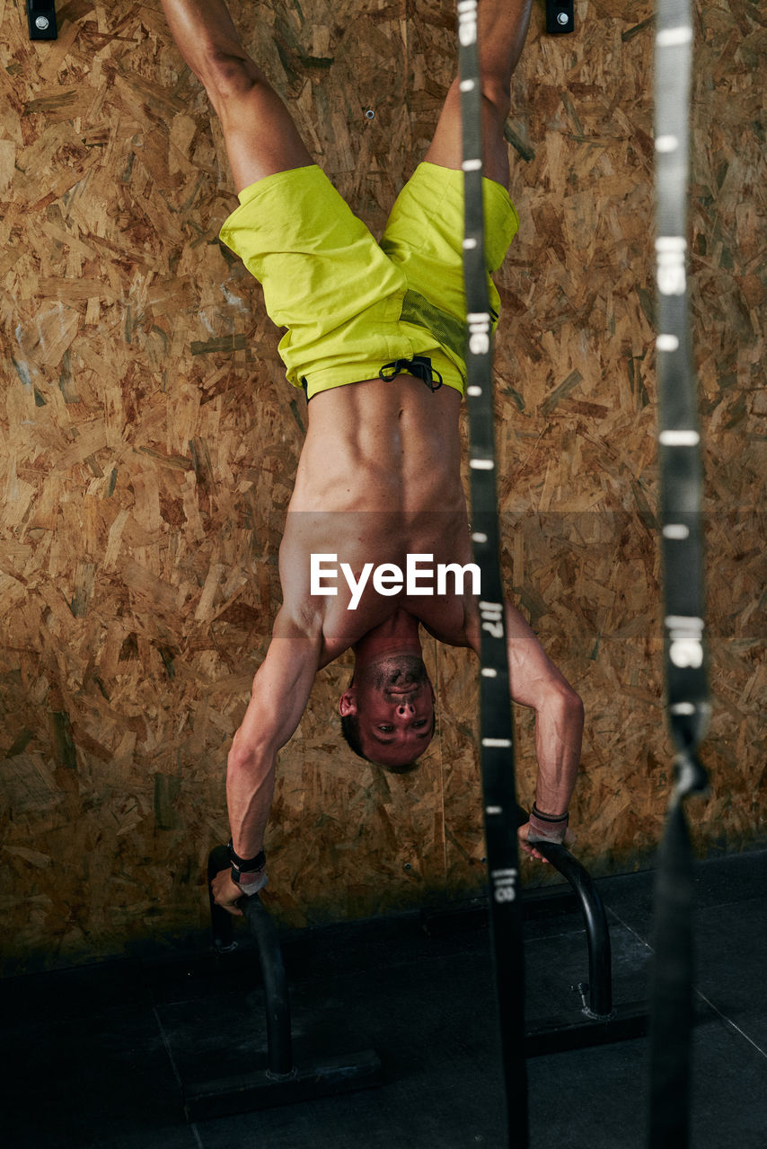 Upside down young fit man doing vertical push ups with bars