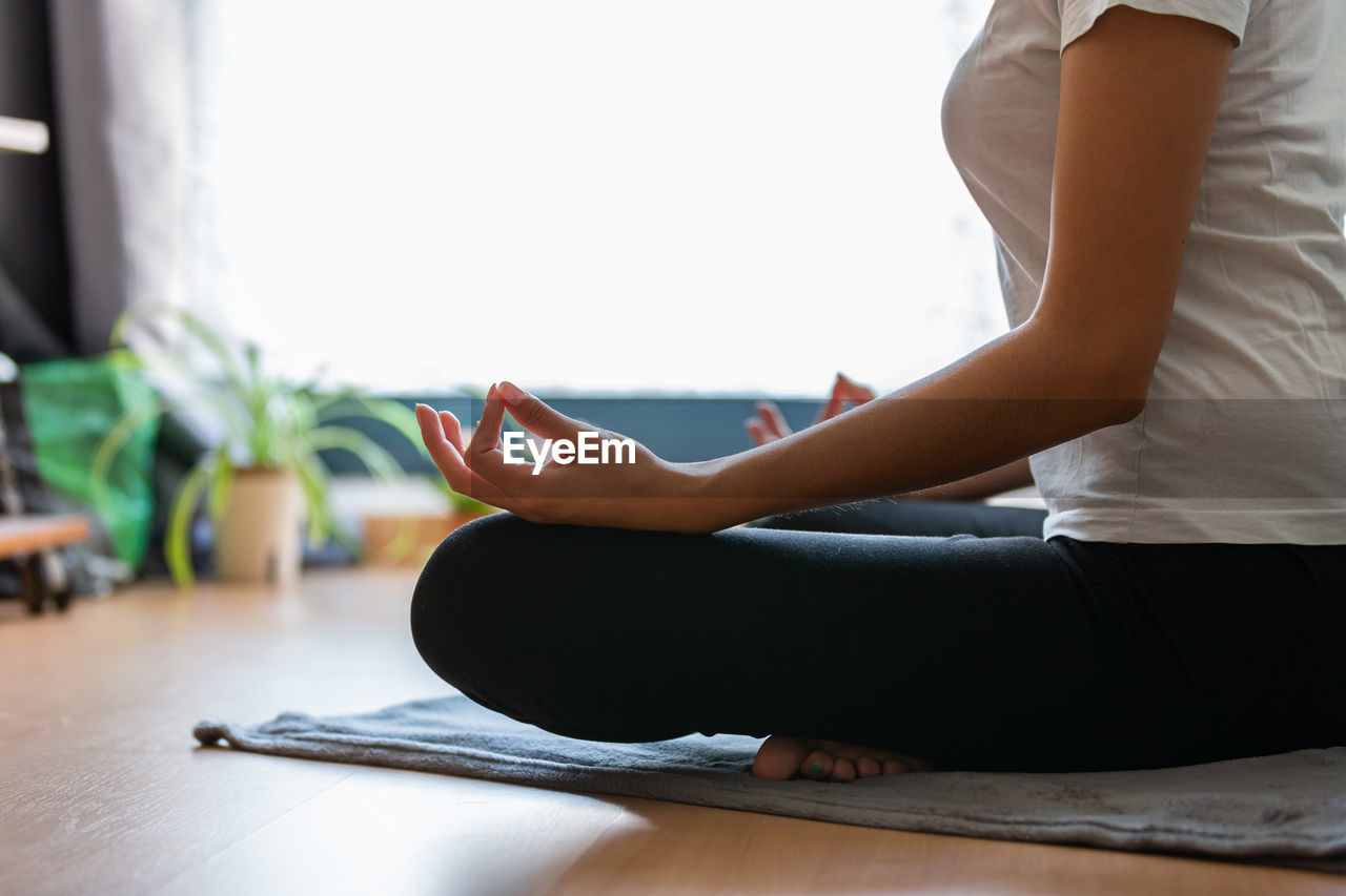 Crop unrecognizable young woman doing yoga at home