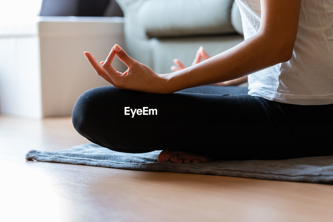 Crop unrecognizable young woman doing yoga at home