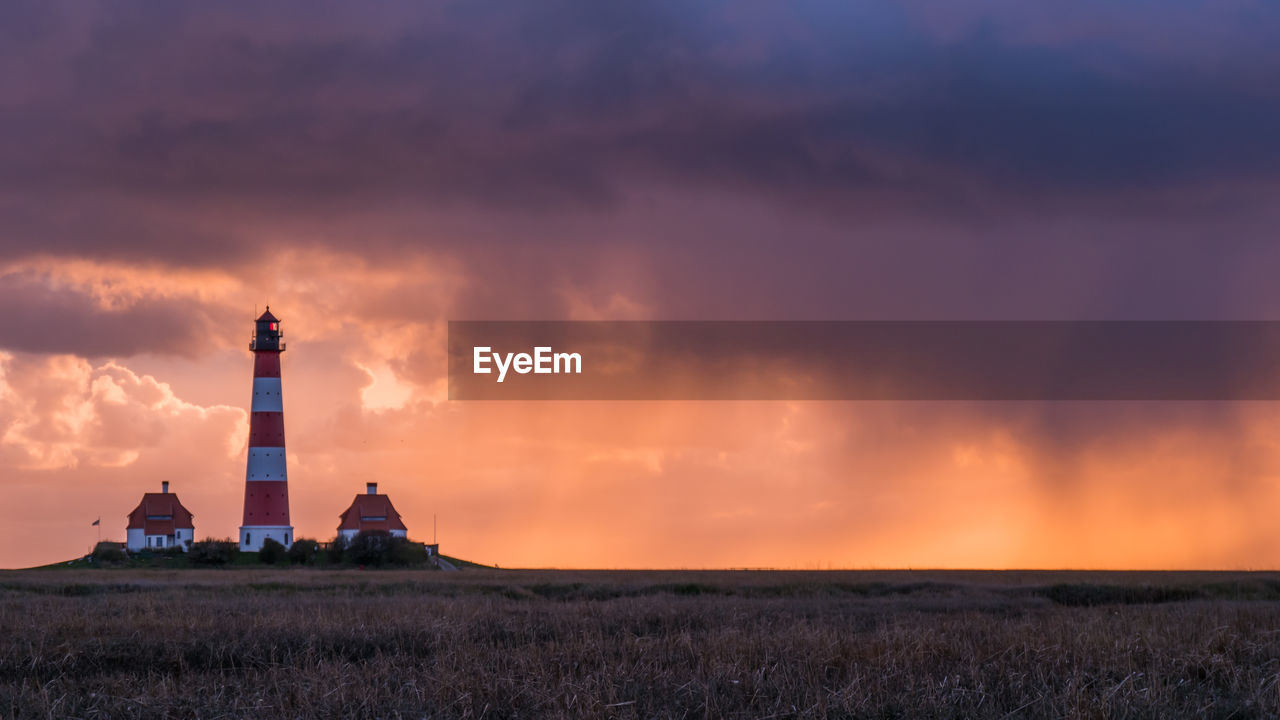 LIGHTHOUSE ON FIELD AGAINST CLOUDY SKY AT SUNSET
