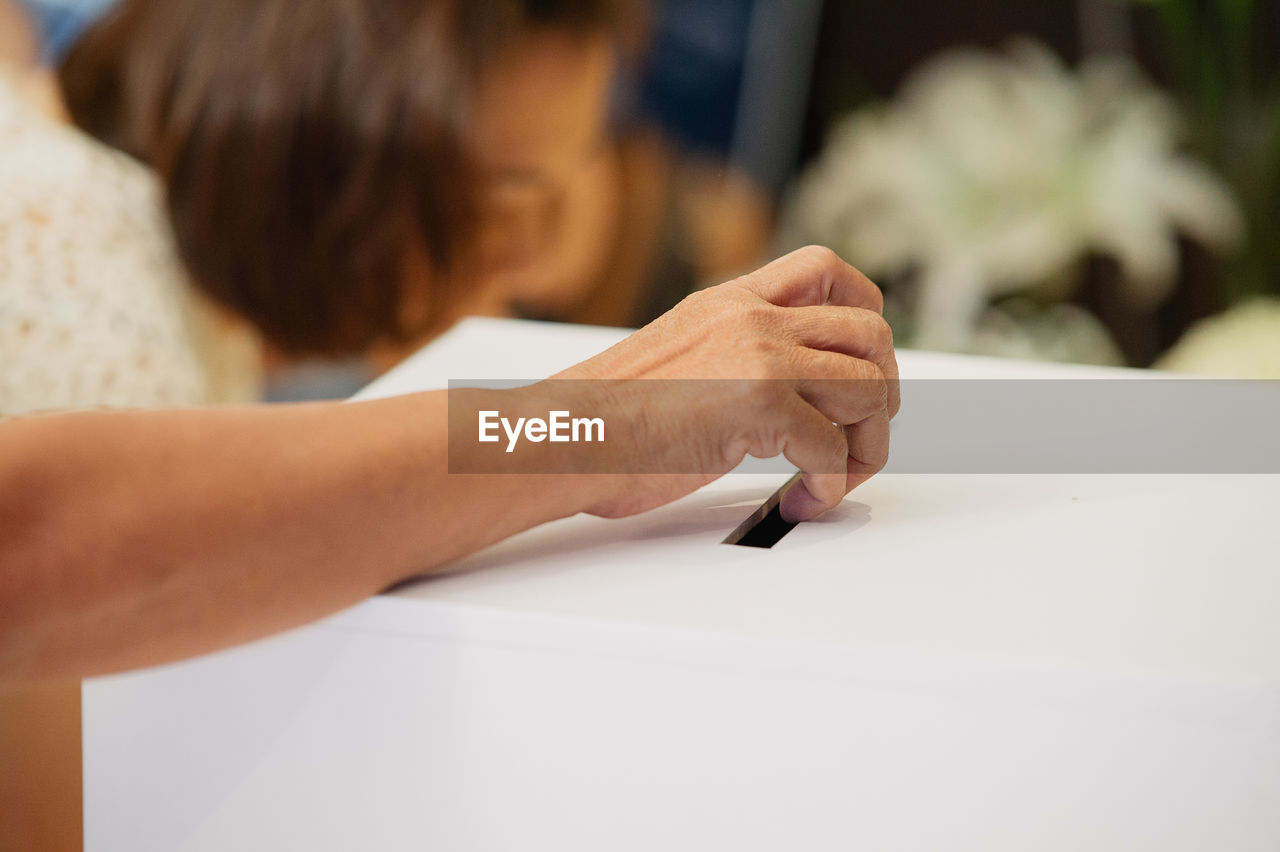 Cropped hand of woman casting vote in ballot box