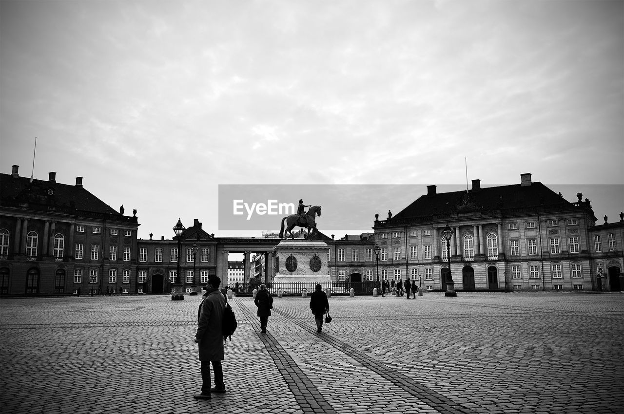 People standing at town square by amalienborg palace against cloudy sky