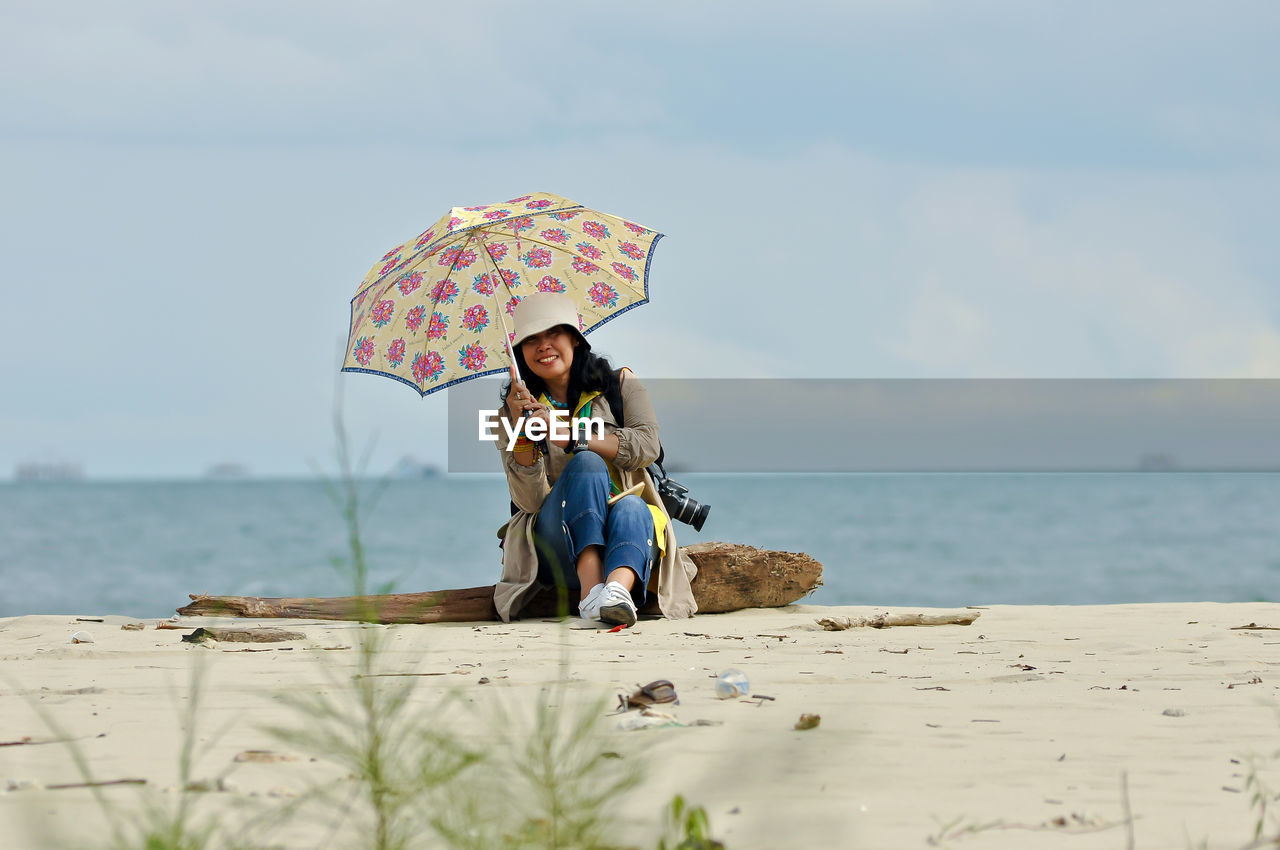 Woman with umbrella on beach against sky