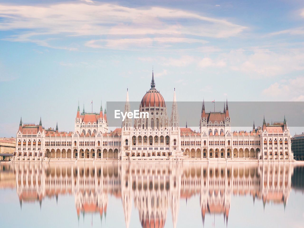 Reflection of hungarian parliament building in river against sky
