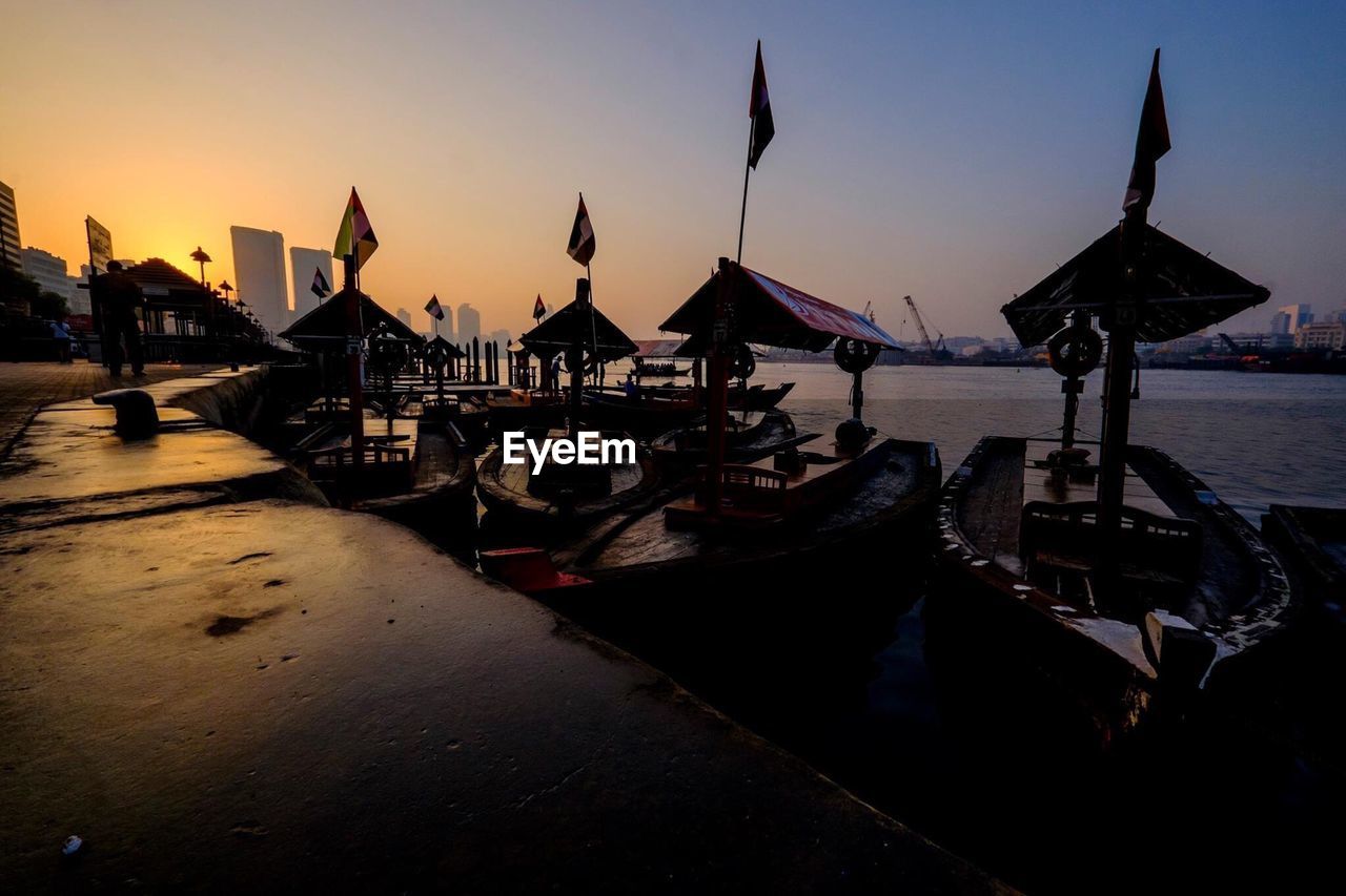 Traditional boats moored at river against sky during sunset