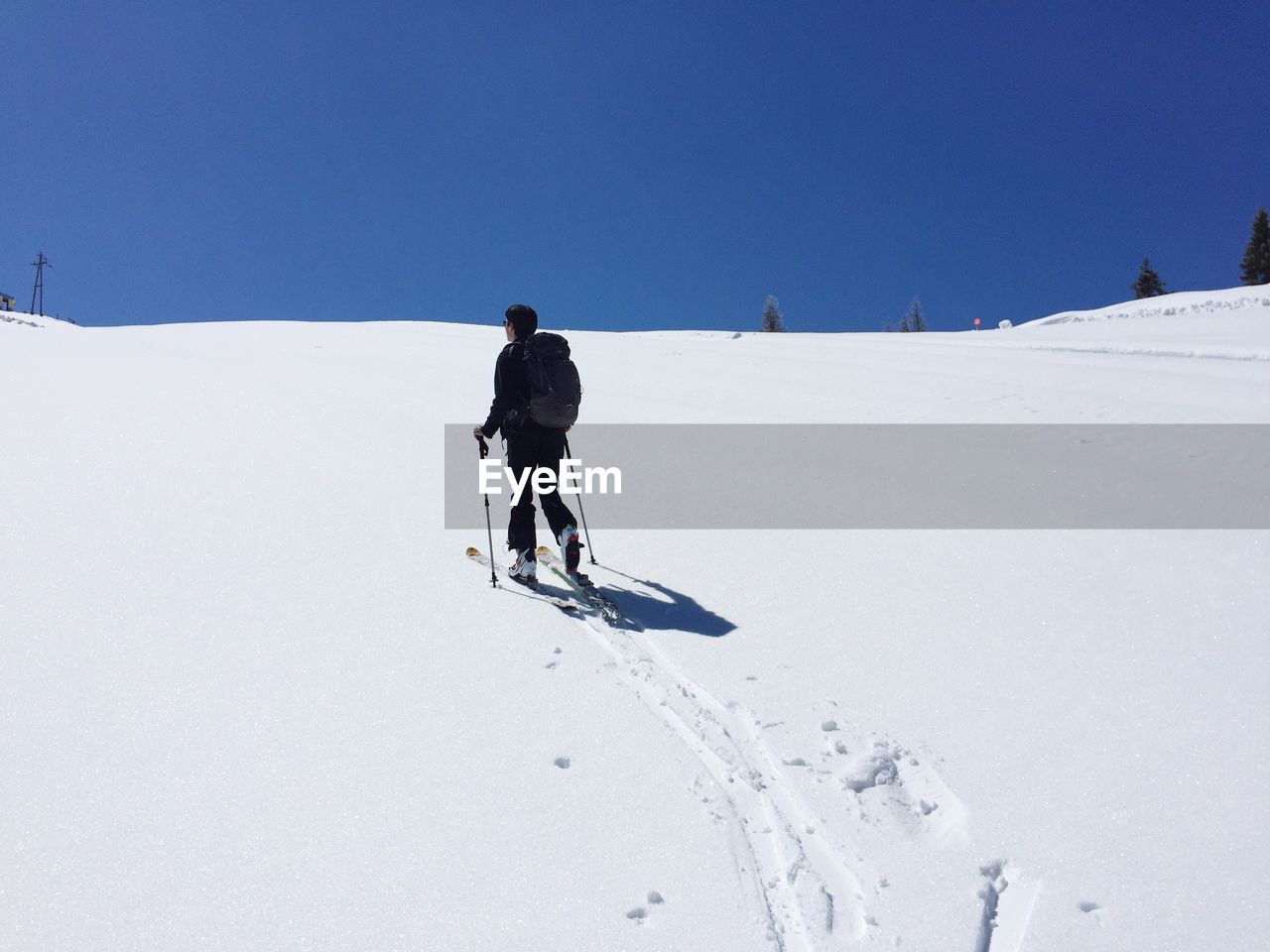 Rear view of person skiing on snow covered field against clear blue sky