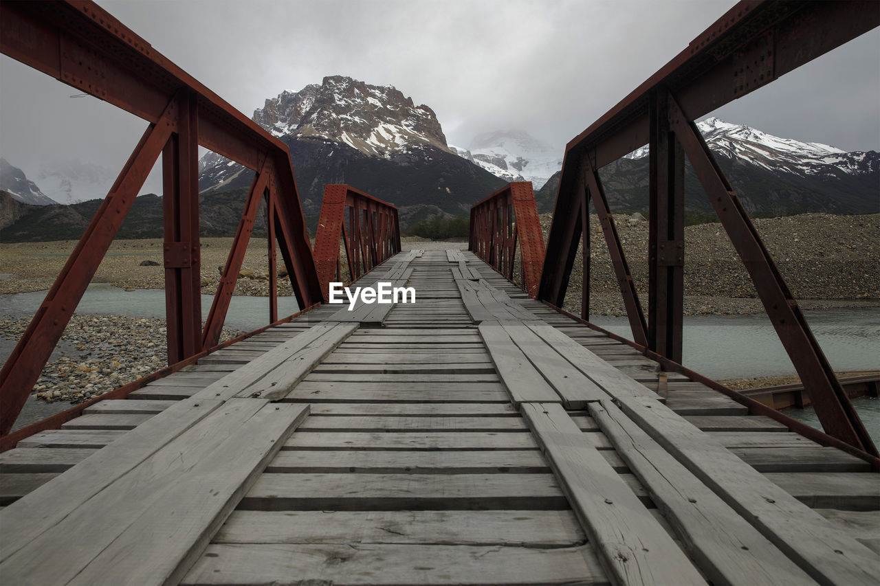 Wooden road bridge crosses river with view of andes mountains, near el chalten, patagonia, argentina