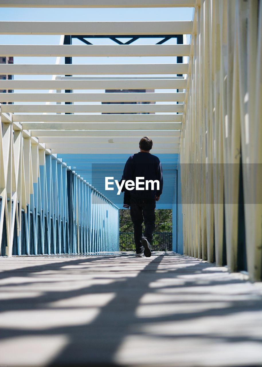 Full length rear view of man walking on footbridge