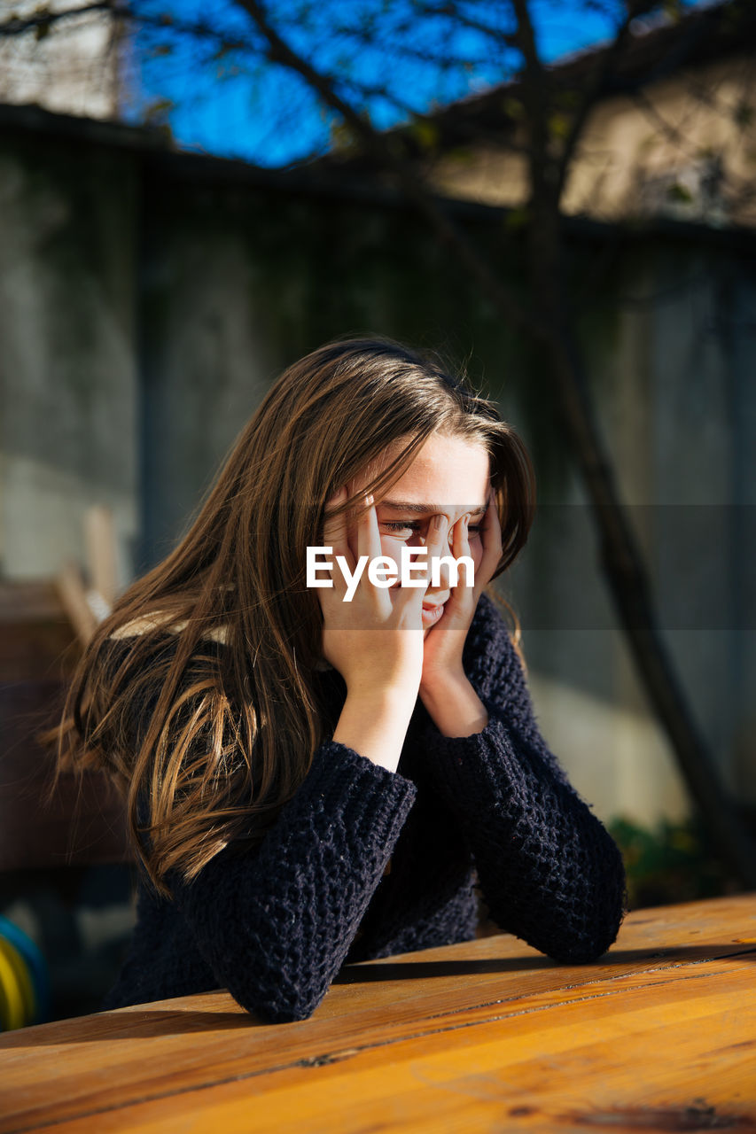 Depressed girl with head in hands sitting at backyard