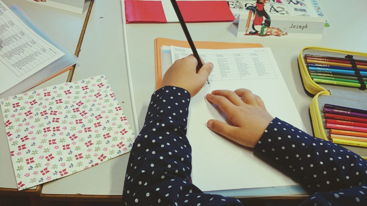 Cropped image of child writing on paper at table