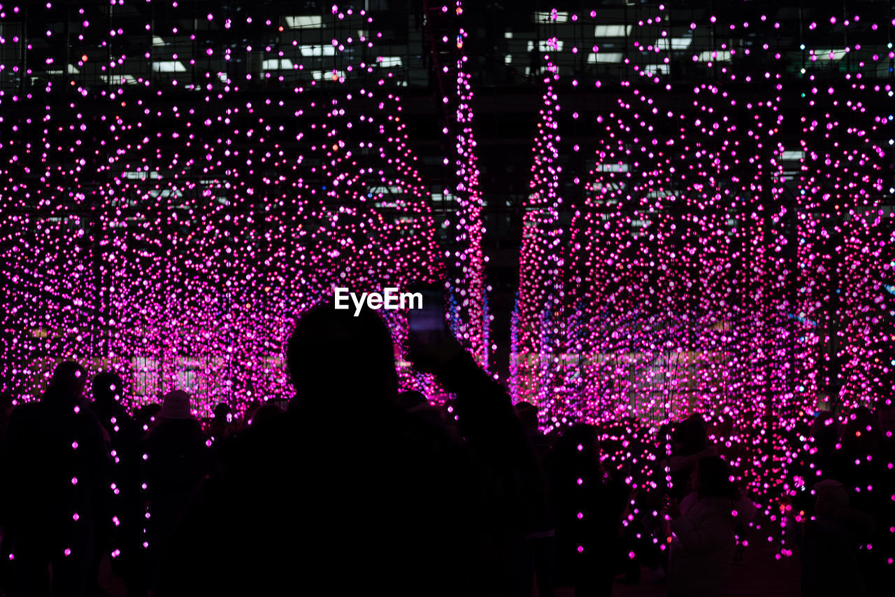 Rear view of silhouette man photographing illuminated pink lights at night