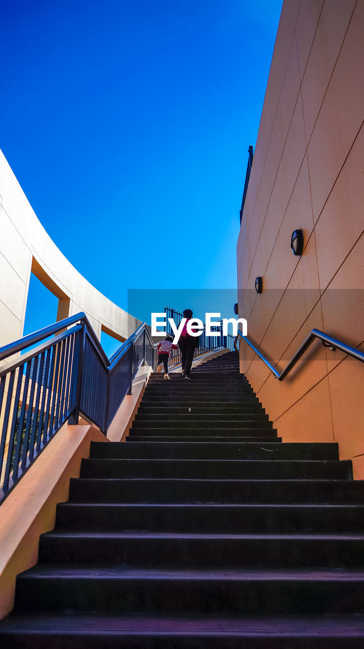 Low angle view of siblings walking on stairs against clear blue sky