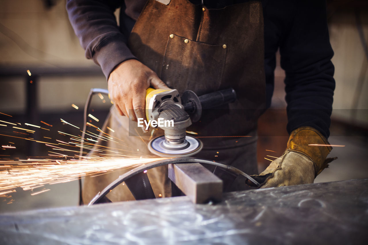 Craftsperson using circular saw while polishing metal at factory