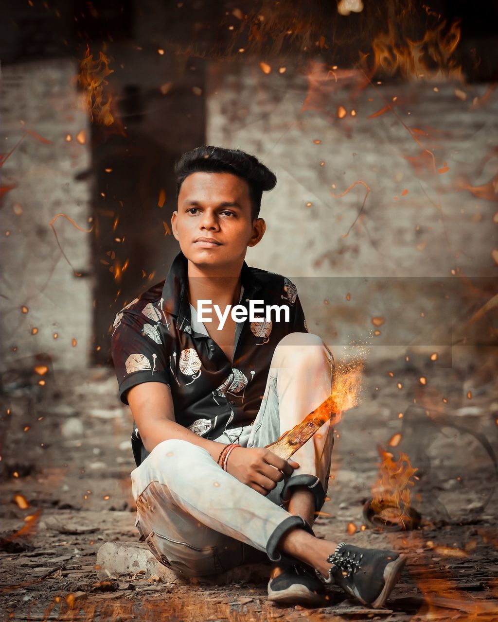 Digital composite image of young man sitting amidst fire