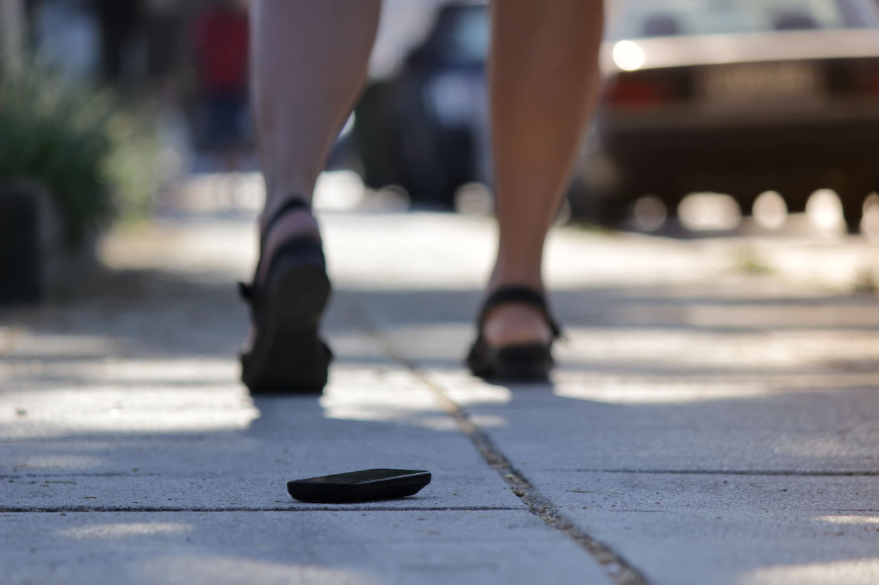 Mobile phone on sidewalk with woman walking in background