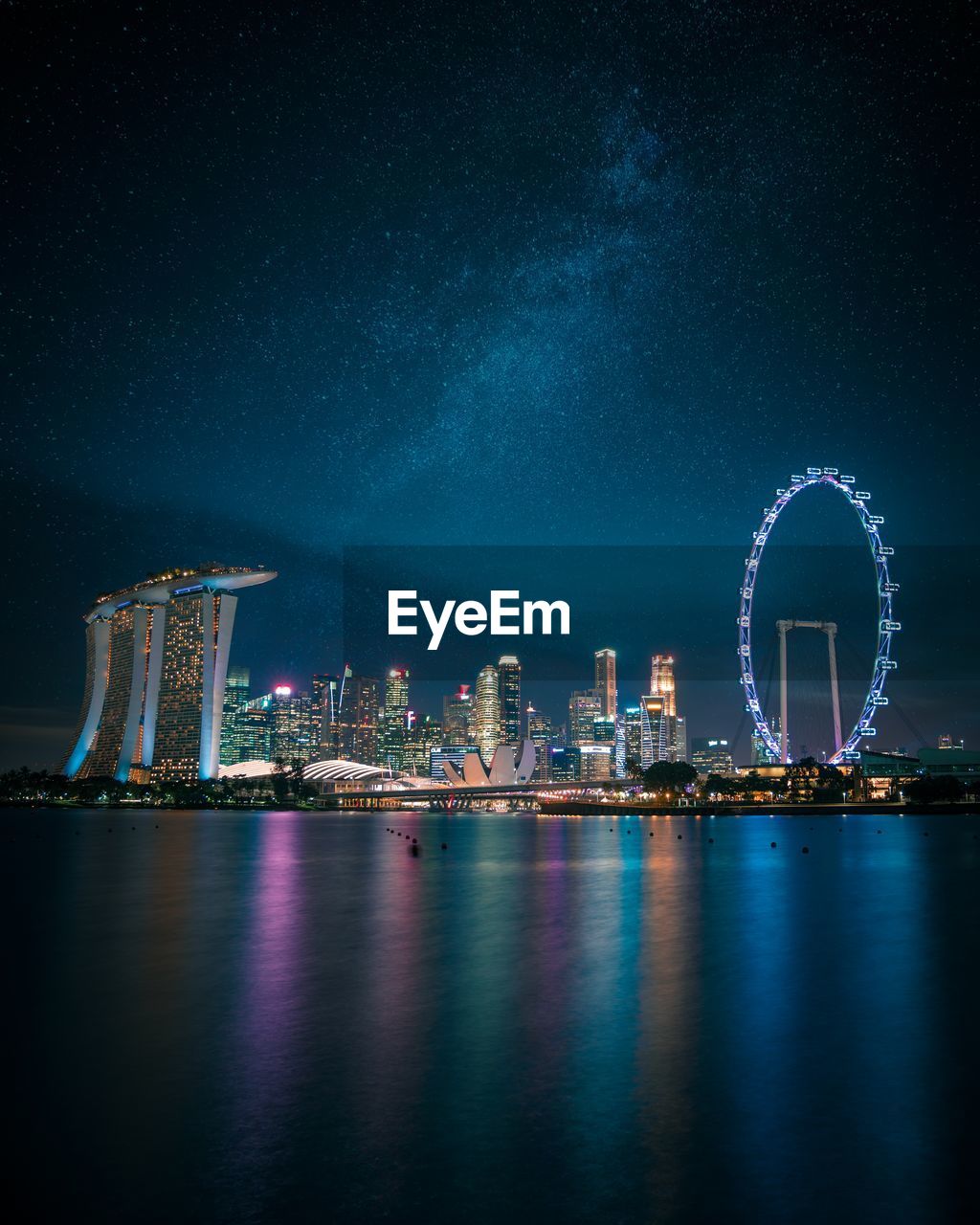 Illuminated marina bay sands and buildings with ferris wheel against sky at night