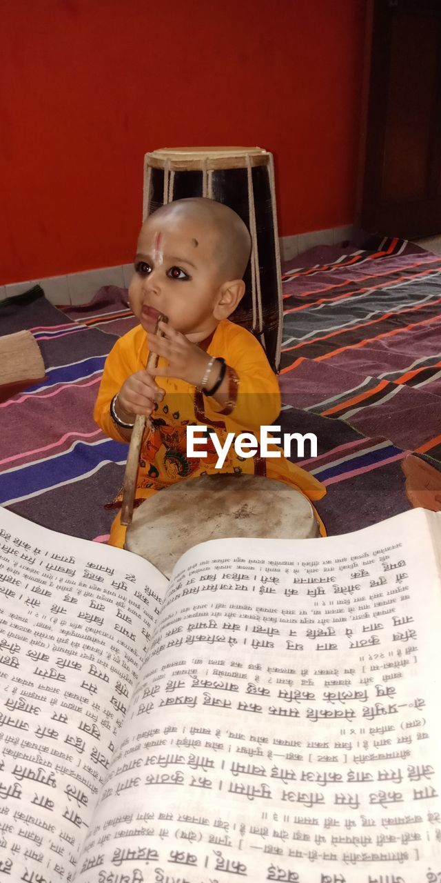 Boy sitting with stick on floor with book at home