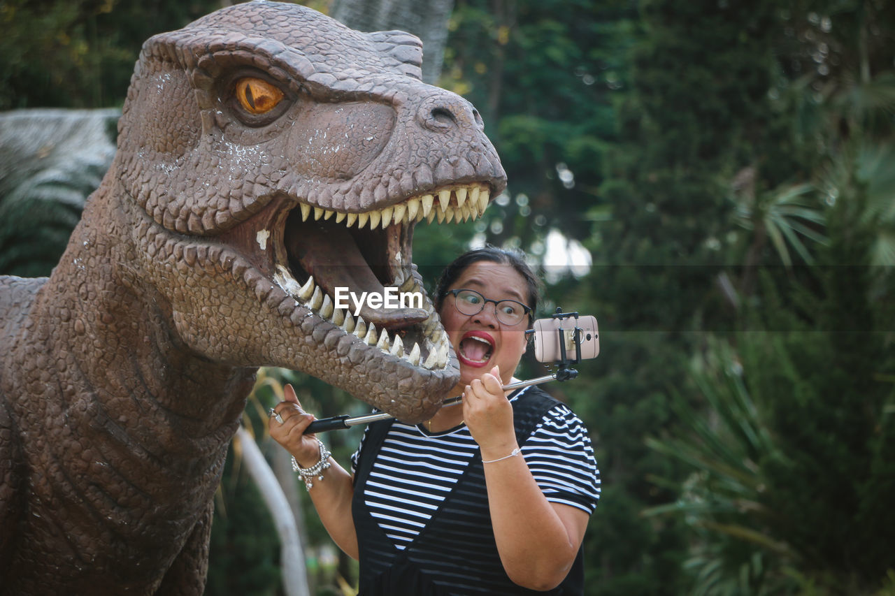 Woman taking selfie with dinosaur statue in park