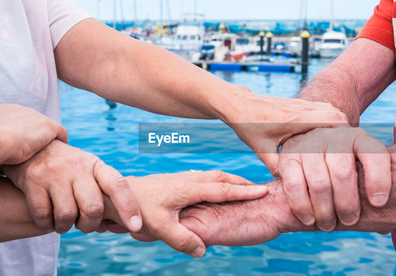 Midsection of senior friends holding hands while standing at harbor