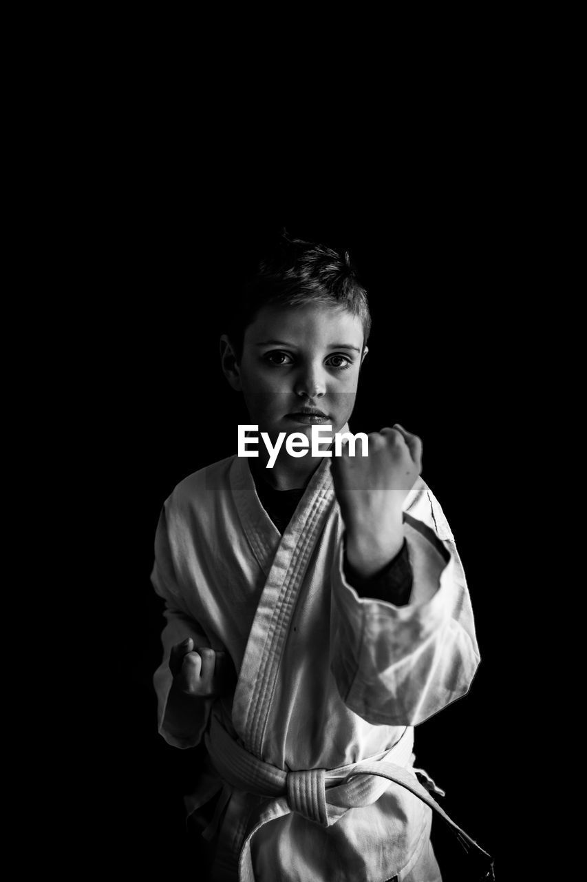Portrait of boy learning martial arts against black background