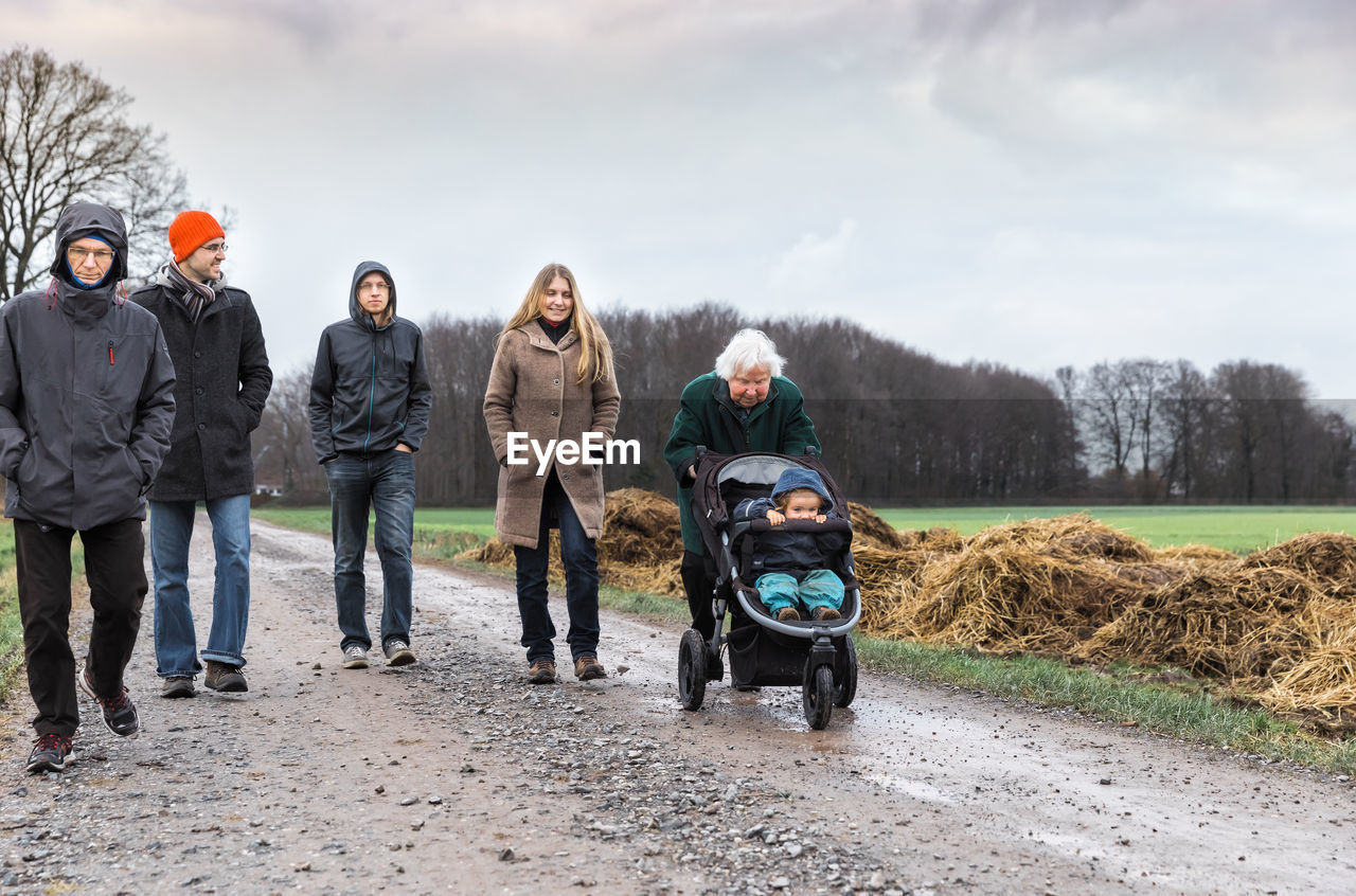 Family walking on dirt road against sky