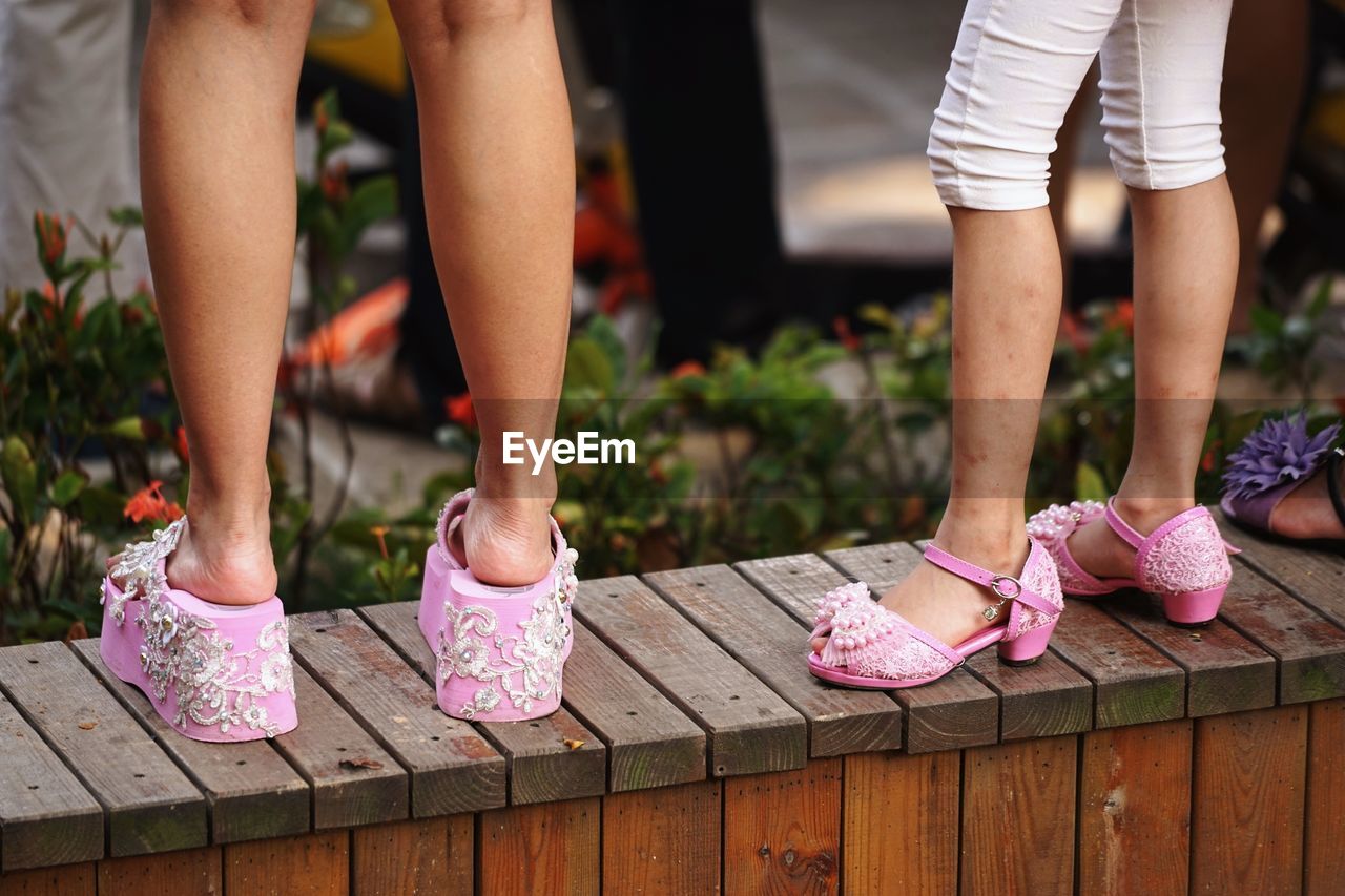 Low section of girls with pink footwear standing on wooden wall