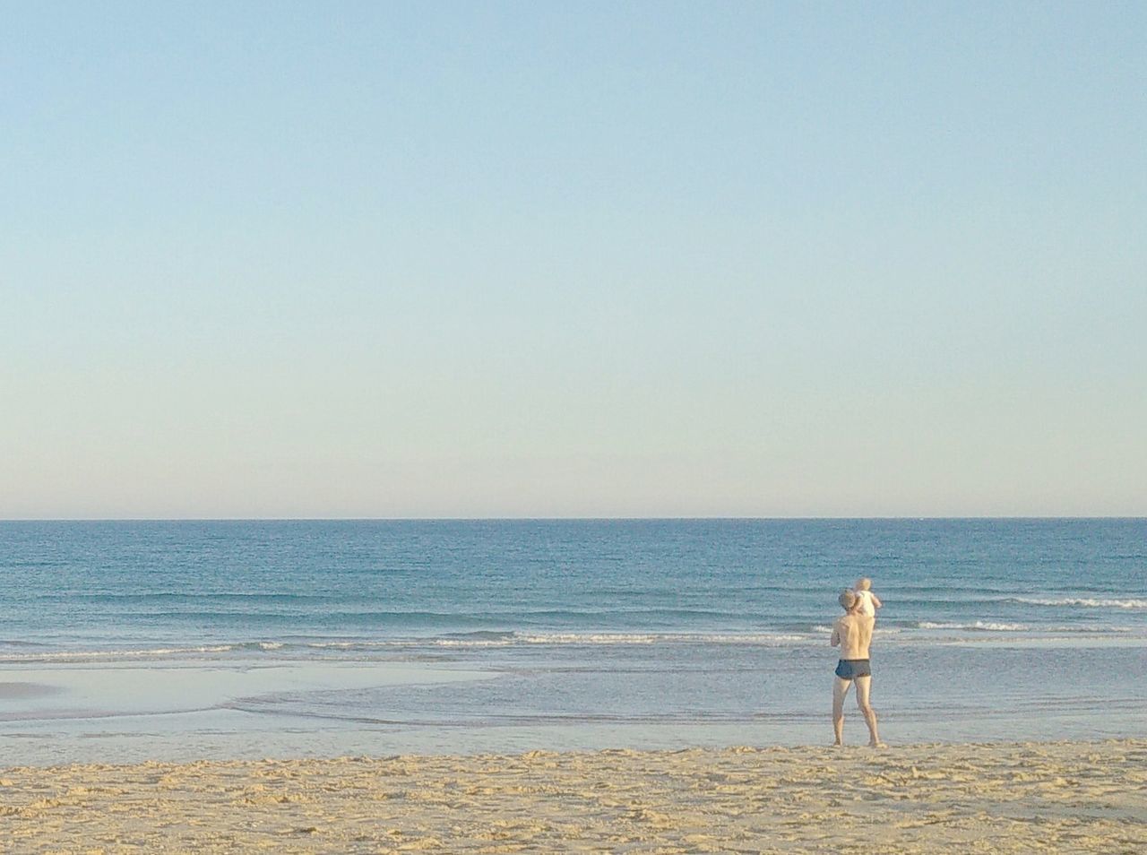 REAR VIEW OF WOMAN STANDING ON BEACH AGAINST SKY