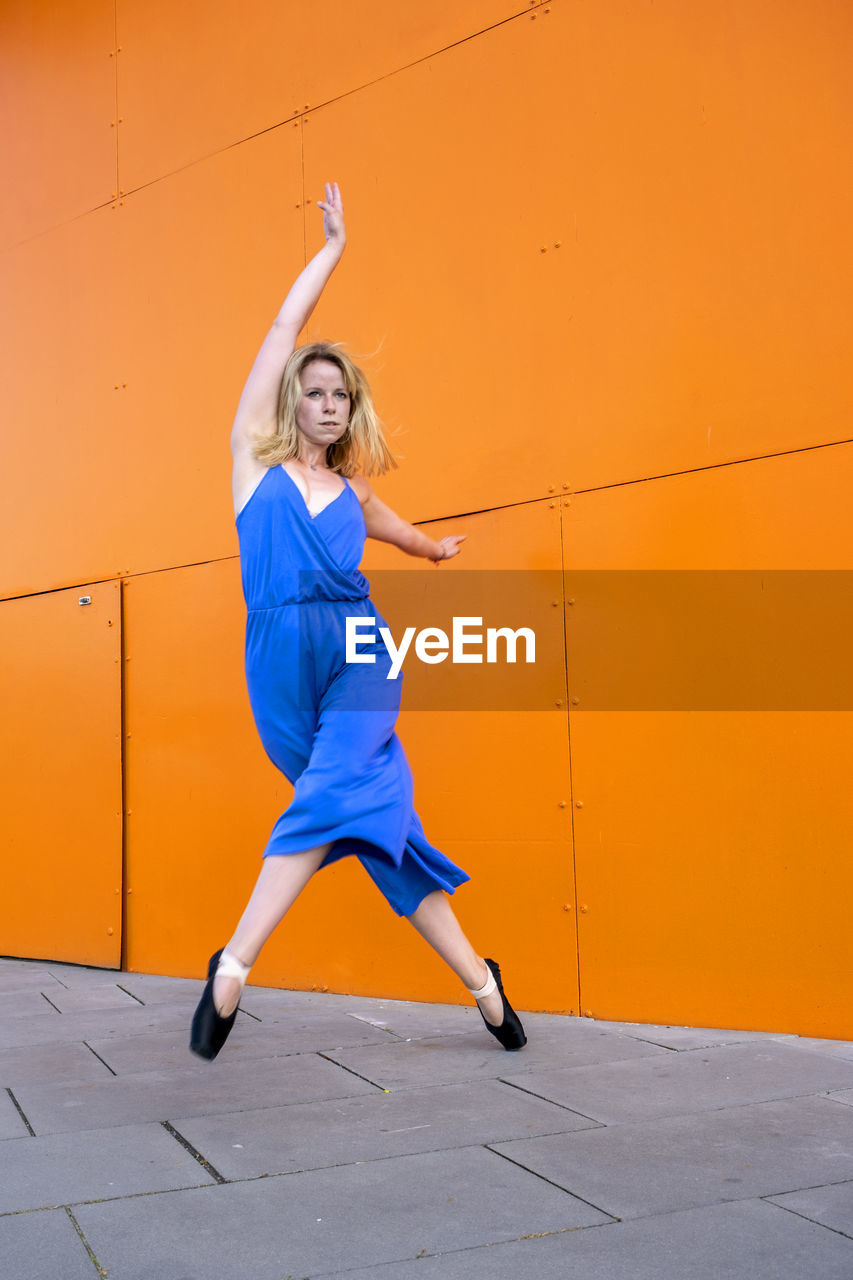 Full length of woman jumping against orange wall