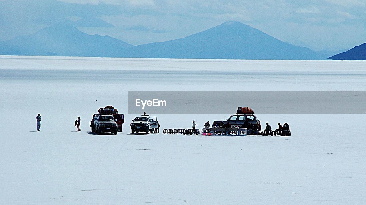 Vehicles and people on snow covered field against mountains