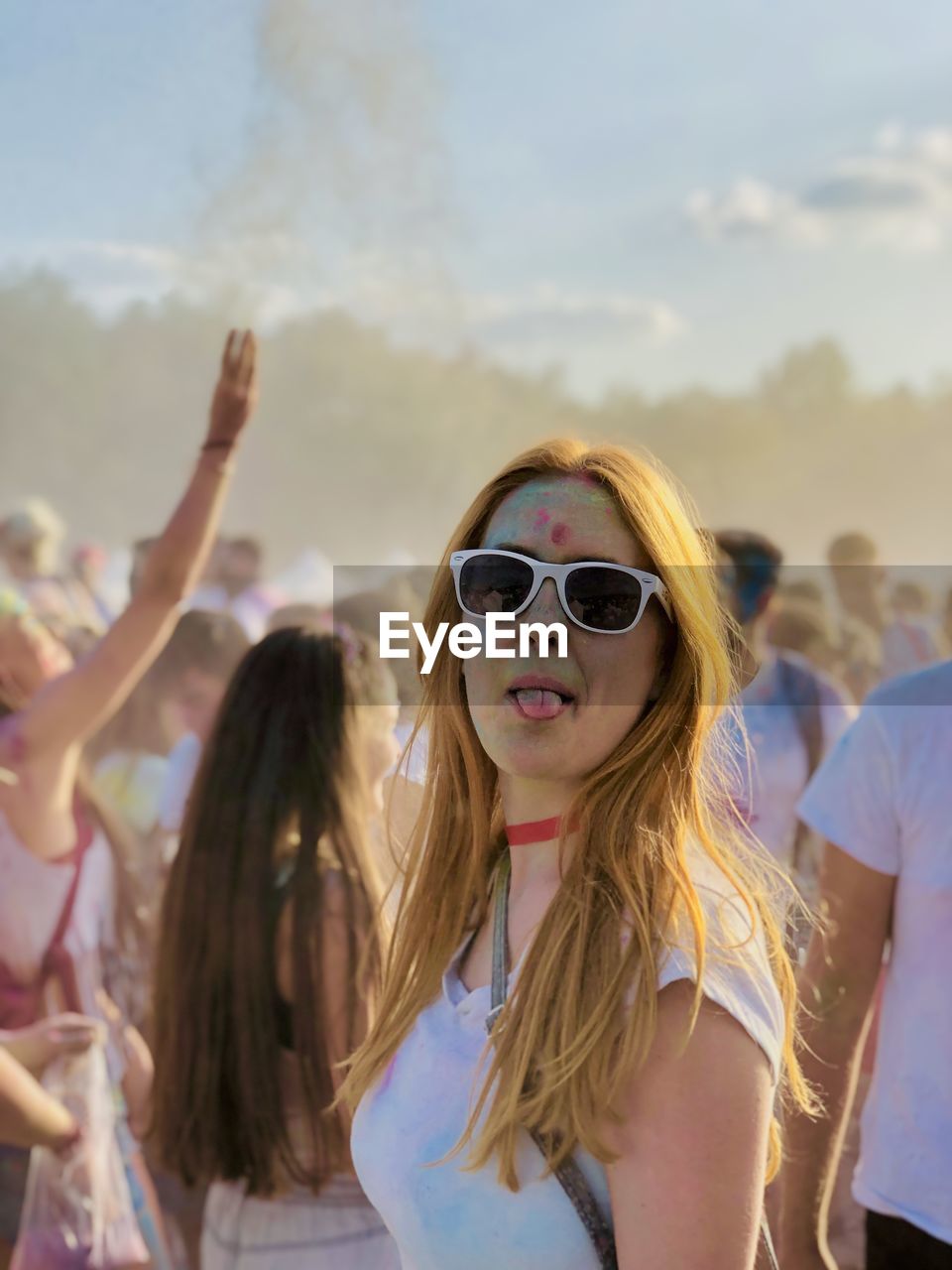 Portrait of young woman with sunglasses sticking out tongue at music festival