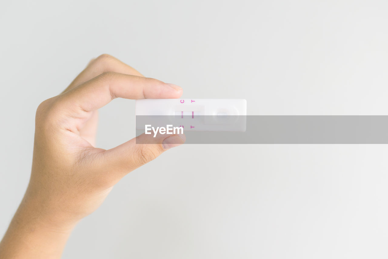 Close-up of hand holding pregnancy test against gray background