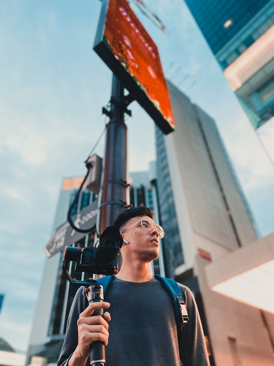 Low angle view of man holding camera standing outside buildings in city