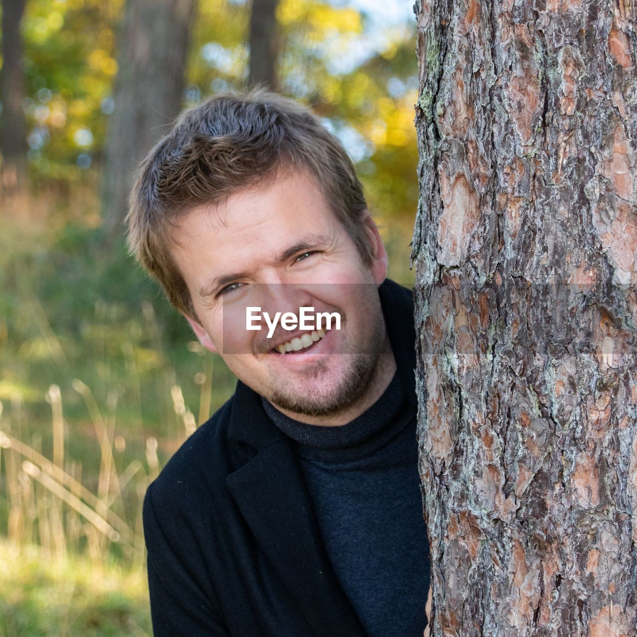 Portrait of smiling young man by tree trunk