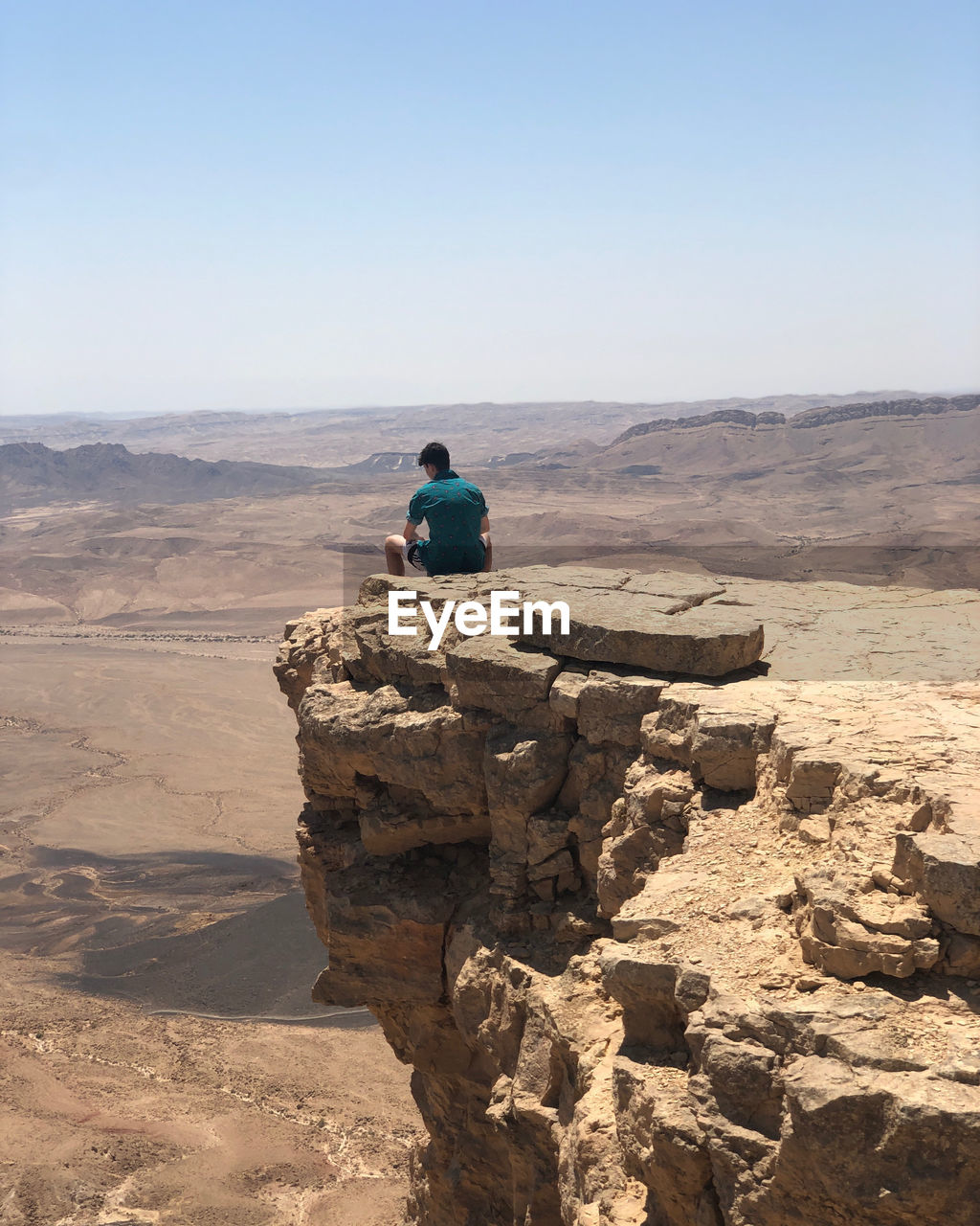 REAR VIEW OF MAN SITTING ON ROCK LOOKING AT VIEW
