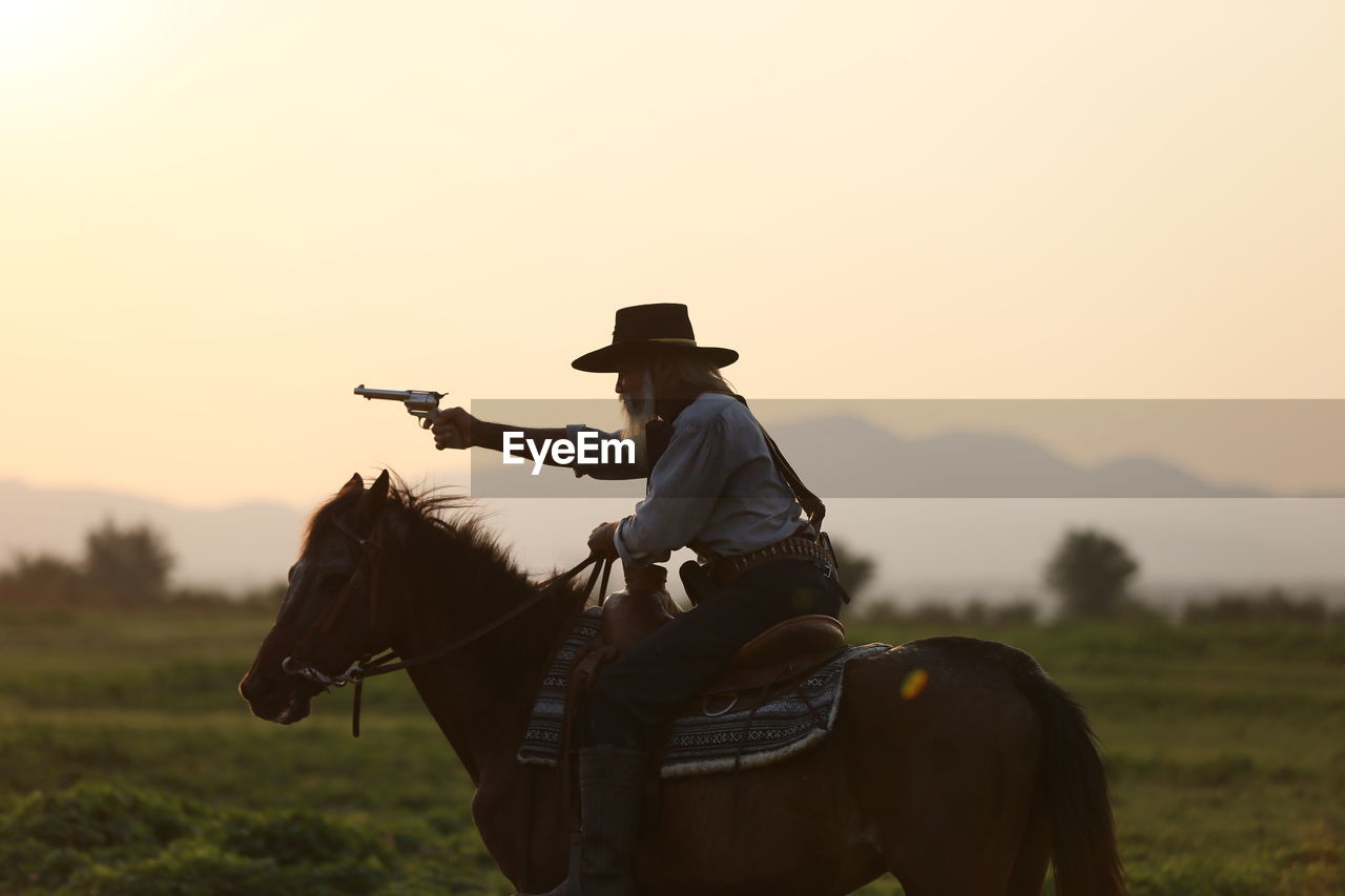 Man riding horse while shooting with handgun against sky