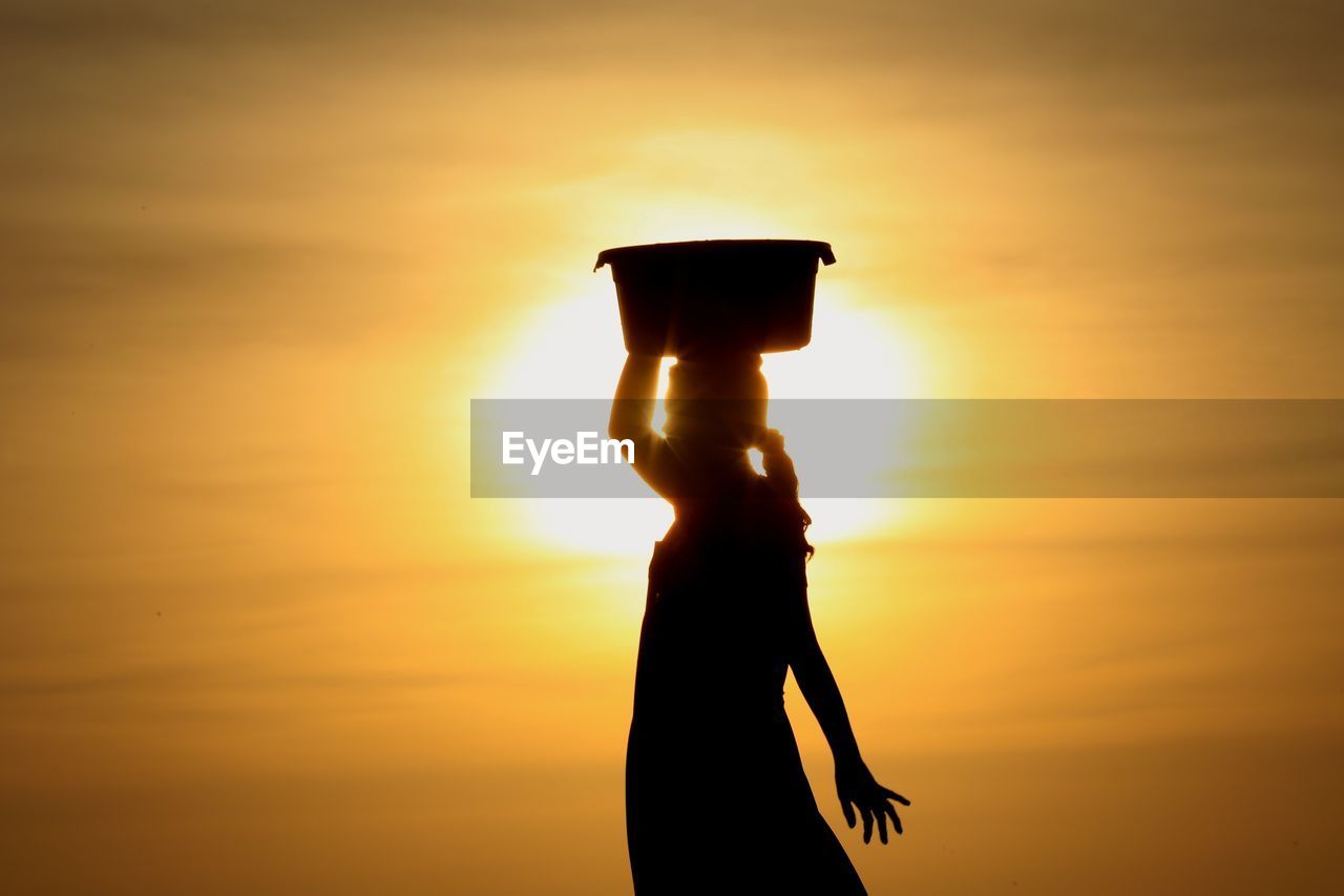 SILHOUETTE WOMAN STANDING ON ORANGE SUNSET