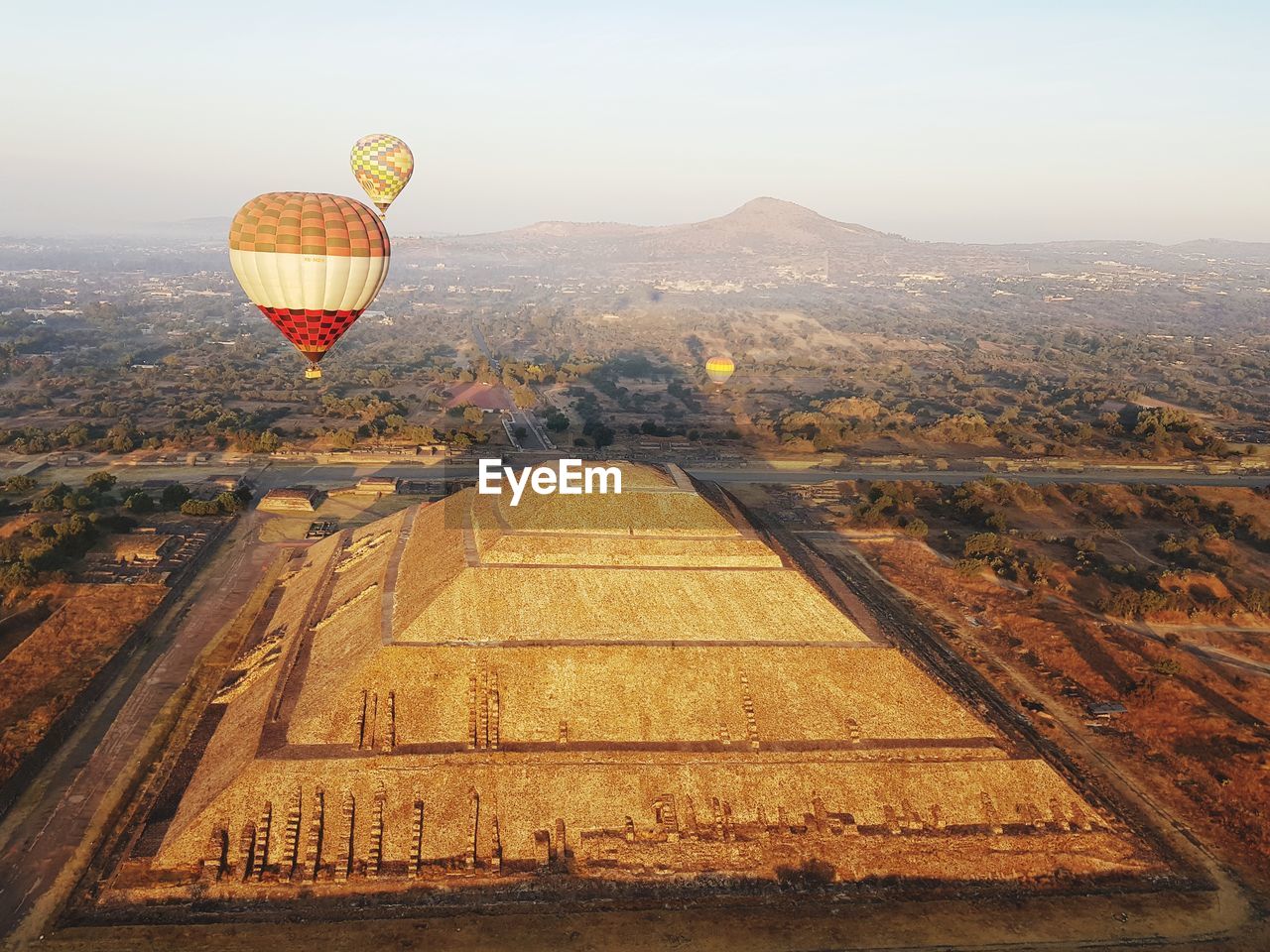 View of hot air balloon flying over landscape and ancient pyramid