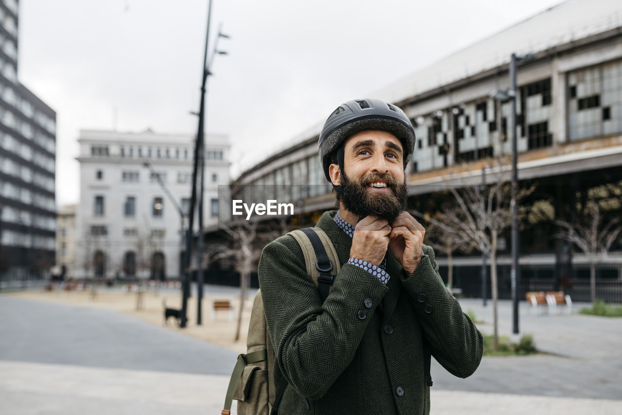 Portrait of smiling man putting on bicycle helmet in the city