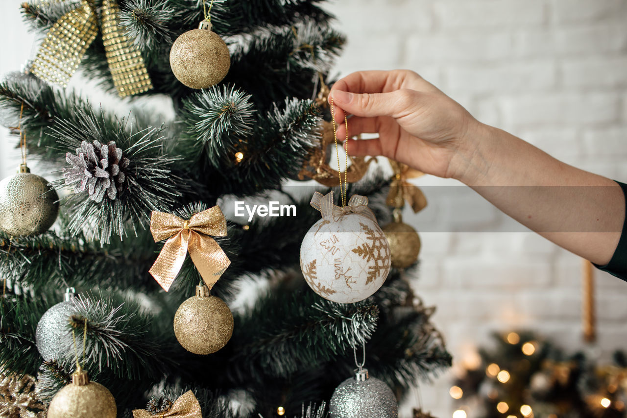 Cropped image of woman holding christmas ornament by tree