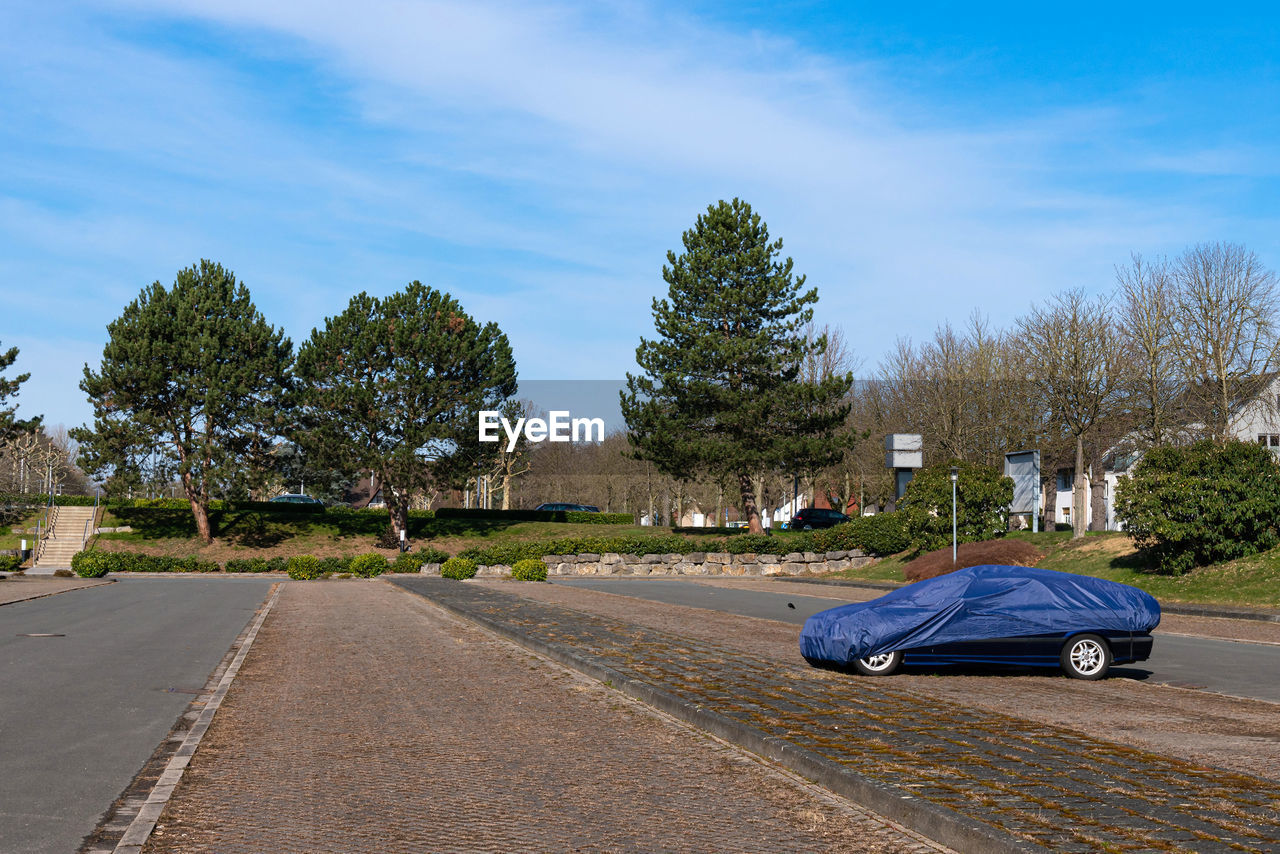 transportation, tree, mode of transportation, road, motor vehicle, plant, sky, car, nature, vehicle, residential area, cloud, blue, city, street, travel, day, no people, land vehicle, outdoors, asphalt, architecture