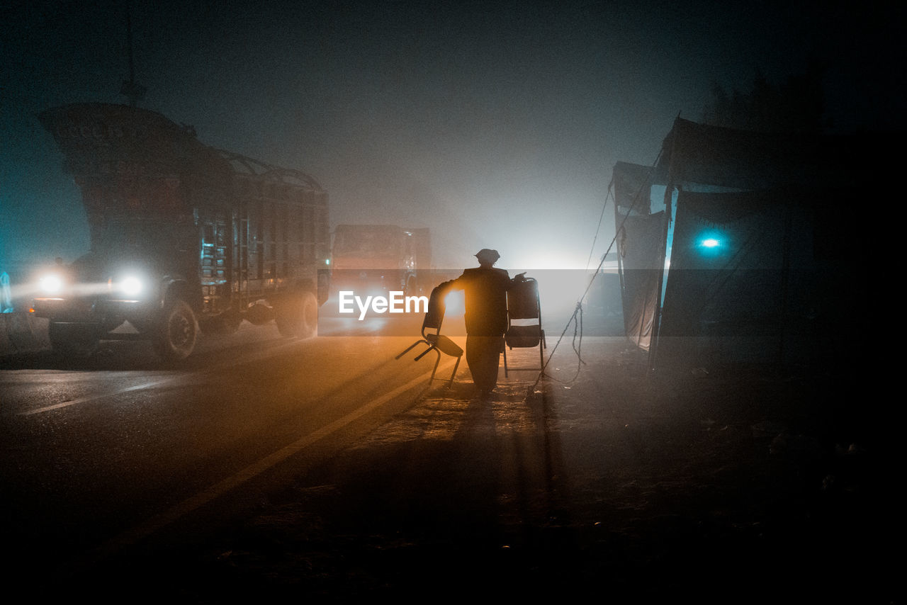 Rear view of man walking on street at night in fog 