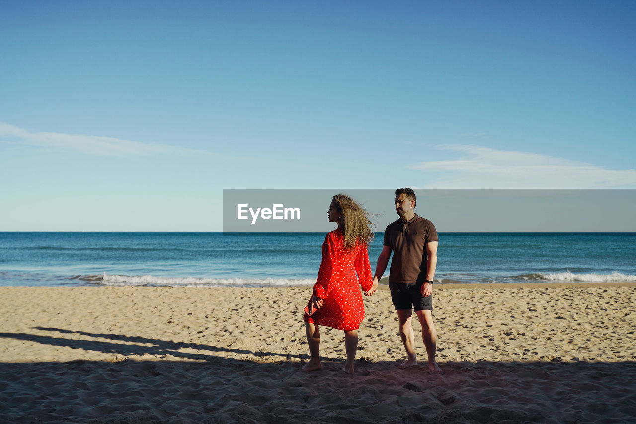 Rear view of woman with man standing at beach against sky